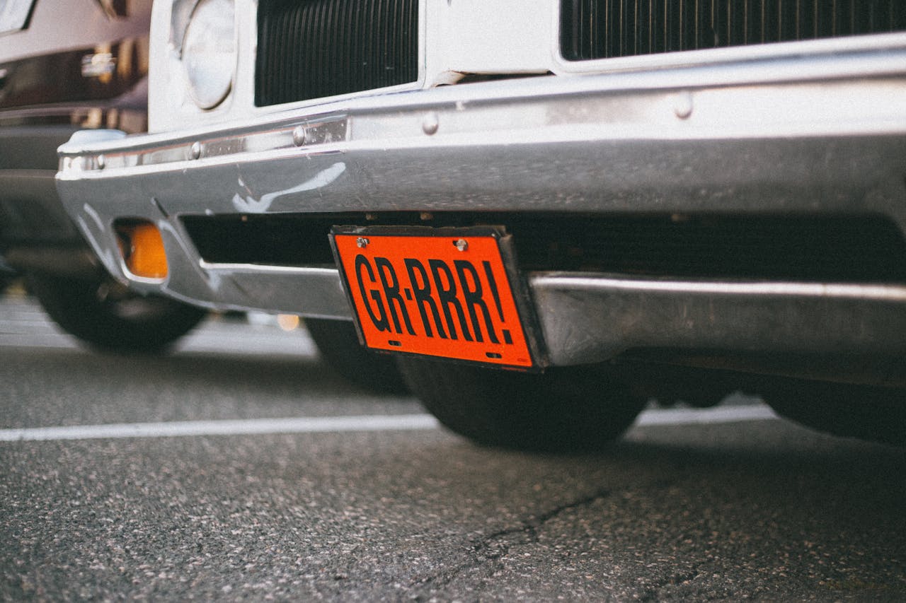 Close-up of a vintage car with a custom orange license plate reading 'GR-RRR!' in a parking lot.
